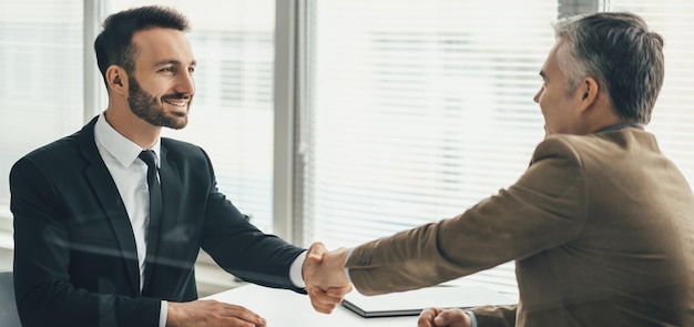 Foto os dois felizes empresários apertando a mão sobre um copo no escritório