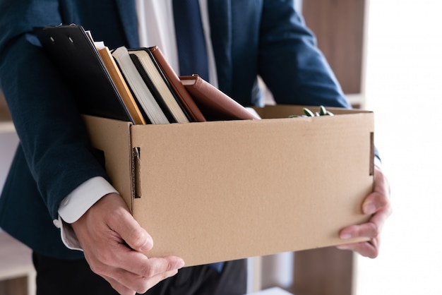 Os empresários estão segurando o documento de demissão e empresa pessoal de embalagem na caixa de papelão marrom, mudando o trabalho, renunciar ao conceito