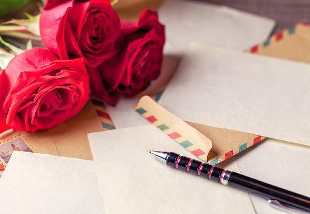 Os envelopes do vintage, a rosa do vermelho e as folhas de papel dispersaram na tabela de madeira para escrever letras românticas.