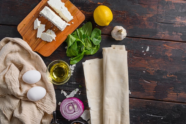 Os espinafres filo dos ingredientes do spanakopita grego eggs a vista superior do feta no espaço de madeira escuro do fundo para o texto.