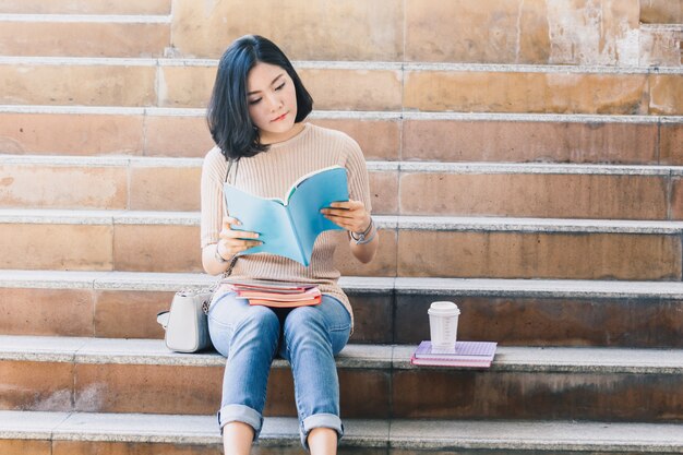 Os estudantes do adolescente da jovem mulher com livros sentam-se na escada