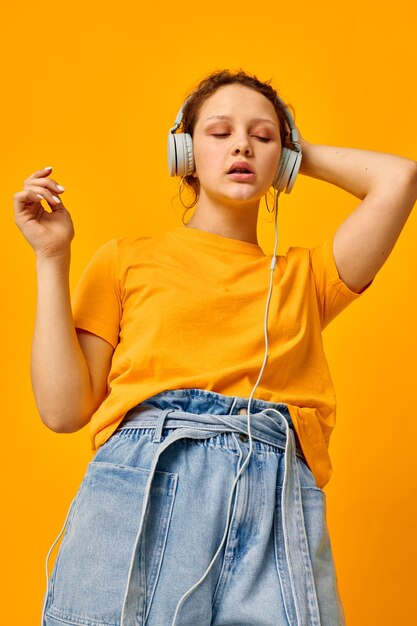 Os fones de ouvido do estilo do verão da menina bonita dançam o fundo amarelo inalterado