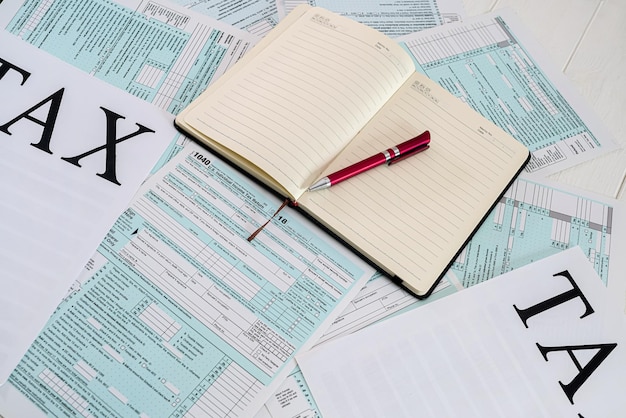 Os formulários de impostos americanos são dispostos em uma mesa ao lado da qual há um caderno com caneta