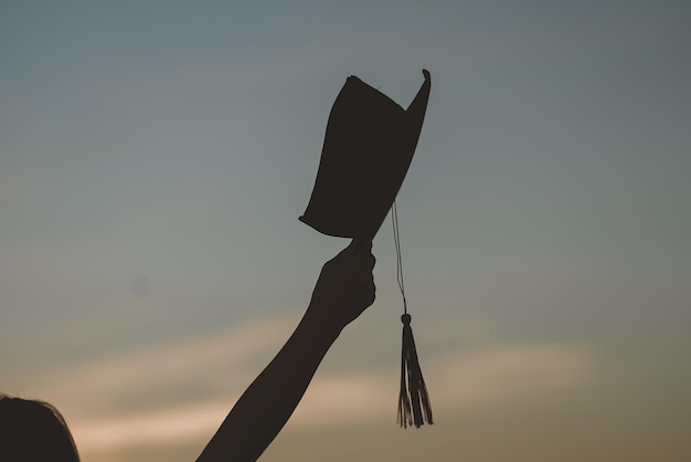 Os graduados usam um chapéu preto para dar os parabéns pela formatura na silhueta do pôr do sol