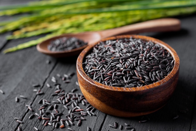 Os grãos de arroz preto em um copo são colocados em uma mesa de madeira preta