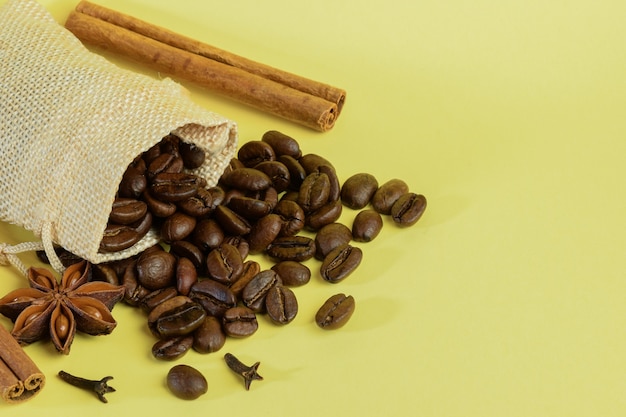 Os grãos de café espalhados de um pequeno saquinho se espalham com erva-doce e canela em um fundo amarelo