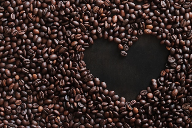 Os grãos de café estão dispostos em forma de coração em uma superfície de madeira escura.
