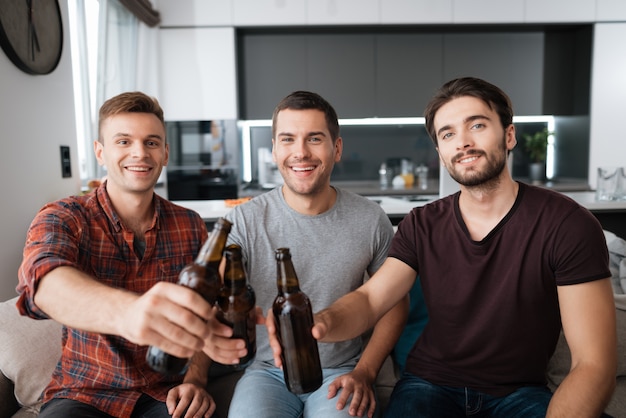 Os homens estão sentados no sofá e bebem cerveja de garrafas