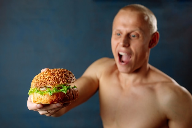 Os homens jovens fortes atletas musculares olham cheeseburger saudável hambúrguer fast-food. coma proteína de hambúrguer