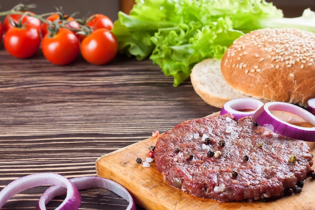 Foto os ingredientes crus para o hambúrguer caseiro na mesa de madeira marrom.