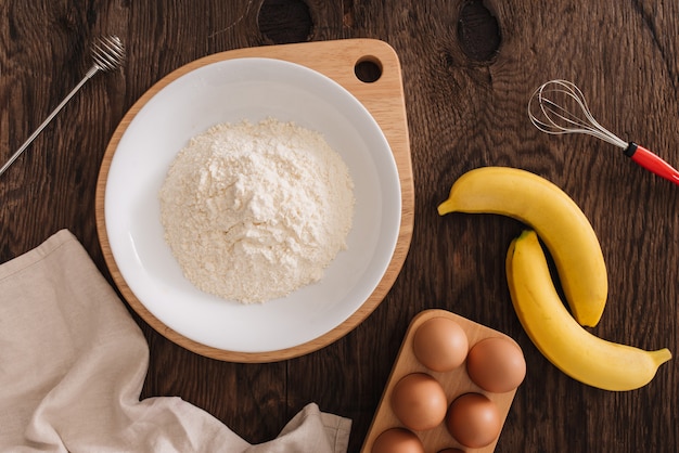 Os ingredientes para o ovo de farinha de bolo de banana na mesa de madeira.