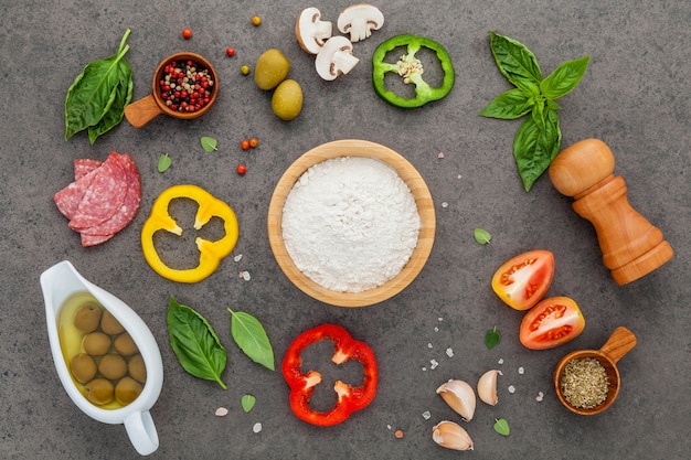 Foto os ingredientes para pizza caseira com ingredientes em fundo escuro de pedra com lay plana.