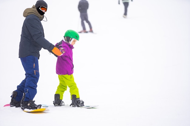 Os instrutores ensinam uma criança em uma encosta de neve a praticar snowboard
