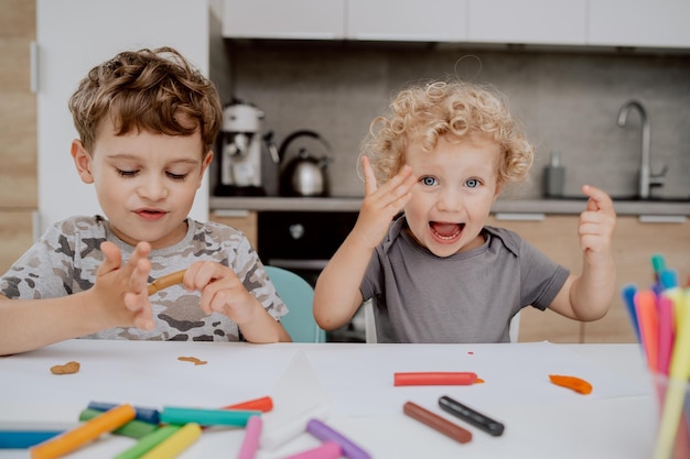 Os irmãos felizes estão sentados à mesa da cozinha brincando com plasticina um menino em idade escolar e um ap