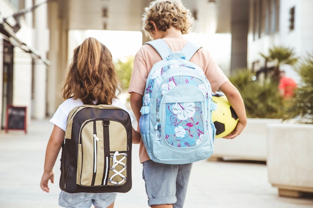 Os irmãos vão à escola com suas mochilas e uma bola de futebol.