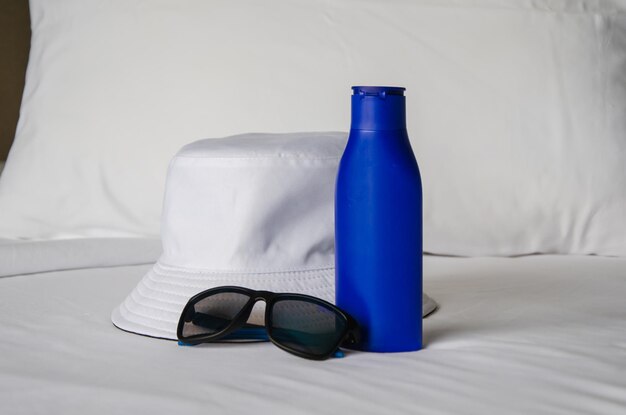 Foto os itens essenciais para proteção solar: loção solar, óculos de sol, chapéu, chapéu de sol e creme uv na cama.
