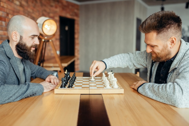 Foto os jogadores de xadrez masculinos começam a jogar, o primeiro movimento. dois jogadores de xadrez começam o torneio intelectual dentro de casa. tabuleiro de xadrez na mesa de madeira, jogo de estratégia