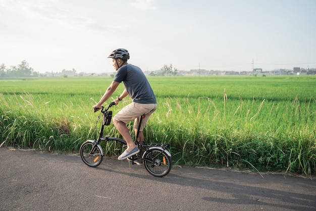 Os jovens asiáticos usam capacetes para andar de bicicleta dobrável nos campos de arroz