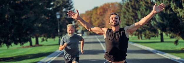 Os jovens e velhos desportistas correndo na estrada