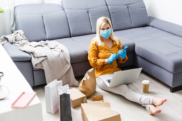 Os jovens em casa em auto-quarentena encomendam produtos de entrega online. Trabalho de casa em quarentena. Nova vida da família mascarada com isolamento do coronavírus. Trabalho remoto em um computador. estilo de vida pandêmico