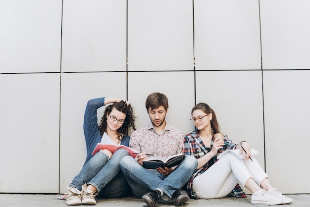 Os jovens estão usando diferentes aparelhos e sorrindo, sentados perto da parede. estudantes que estudam usando o laptop. conceito de mídia social de educação.