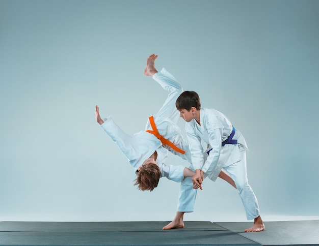 Os meninos adolescentes lutando no treinamento de Aikido na escola de artes marciais. Estilo de vida saudável e conceito de esportes. Adolescentes em quimono branco sobre fundo branco. Crianças com rostos concentrados