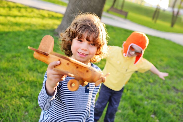 Foto os meninos com cabelo encaracolado jogam um avião de madeira do brinquedo no parque.