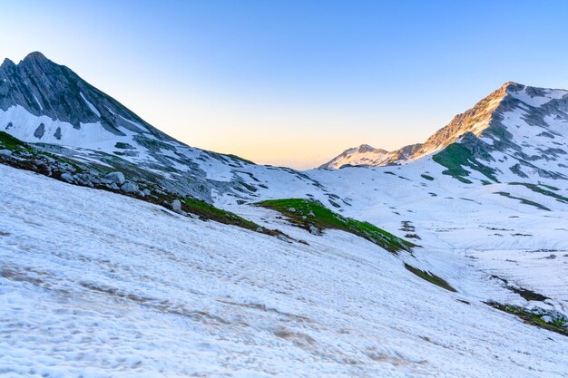 Os montes de neve e grama verde no topo das montanhas na floresta tropical ao nascer do sol