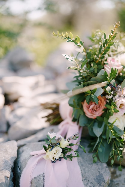 Os noivos brotam de flores brancas contra o fundo de um bouquet de pedras e uma fita rosa