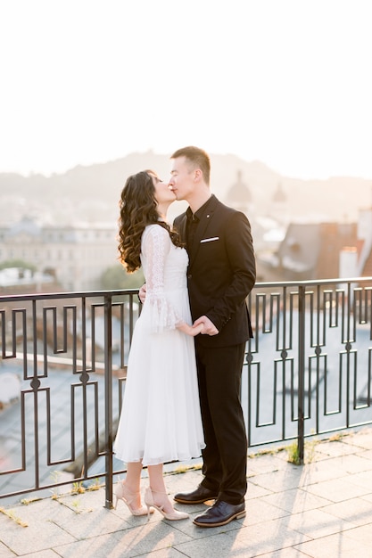 Os noivos novos chineses bonitos dos noivos acoplam o beijo e o abraço no terraço da cidade velha no dia do casamento.