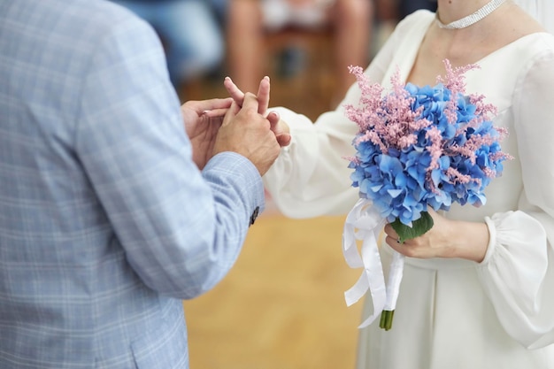 os noivos trocam alianças, a noiva segura um buquê de hortênsias azuis e flores secas na mão