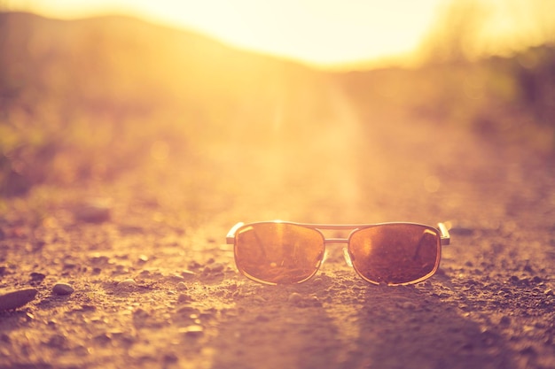 Os óculos de sol do conceito de aventura nas férias de verão estão no chão de uma estrada rural fechada