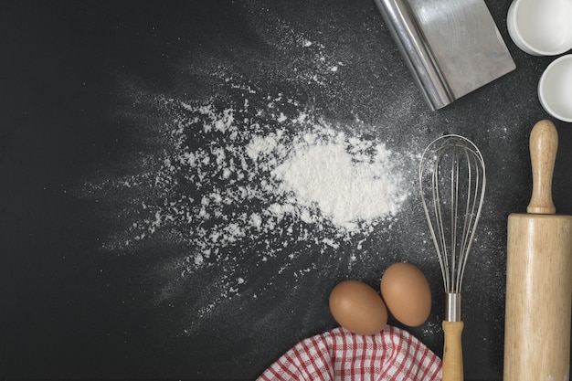 Os ovos com uma xícara de farinha e bata na mesa preta de farinha