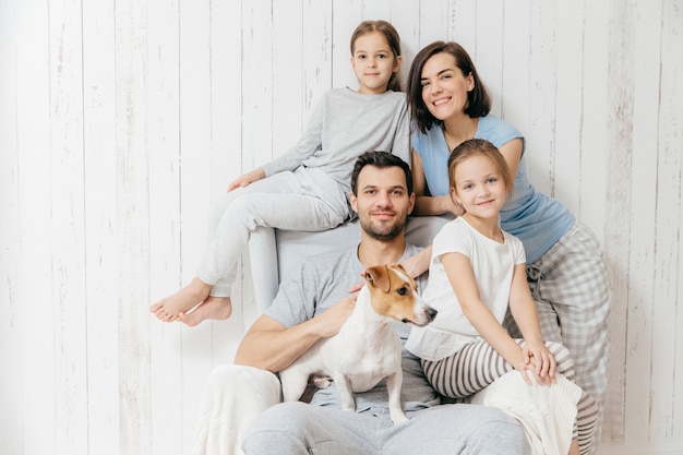 Os pais felizes com suas duas filhas e cachorro posam juntos contra branco