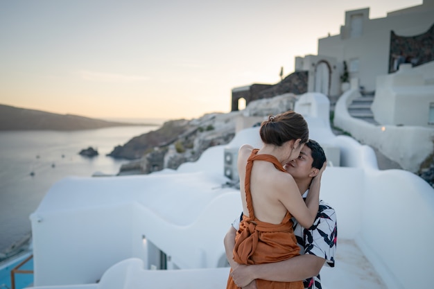 Os pares asiáticos que beijam e que apreciam veem a vila de Oia na ilha de Santorini, Grécia.