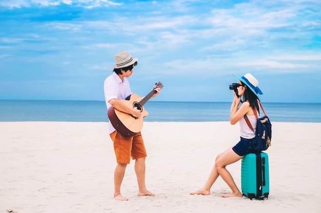 Os pares de viajante têm uma bagagem e estão jogando a guitarra na praia.