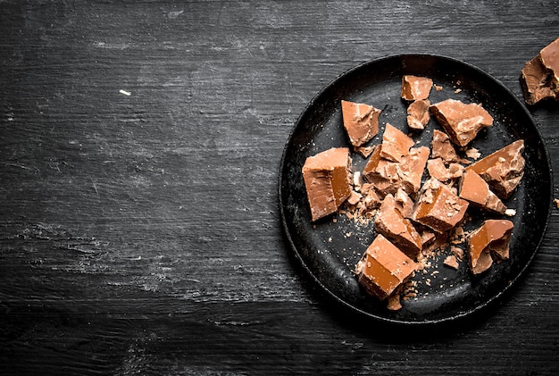 Os pedaços de chocolate no prato velho em um fundo preto de madeira