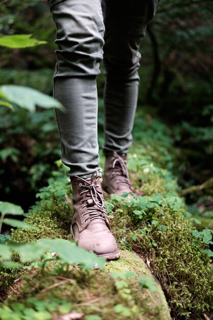 Os pés da mulher em botas de viagem em um tronco musgoso na floresta. Conceito de viagens.