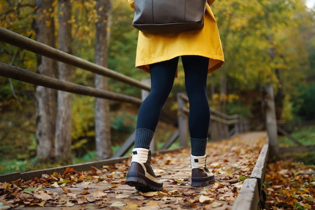 Os pés das mulheres em botas percorrem um caminho de madeira na floresta de outono