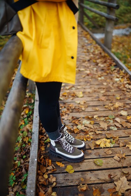 Os pés das mulheres em botas percorrem um caminho de madeira na floresta de outono