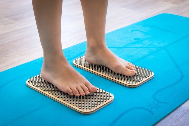 Os pés das mulheres estão de pé em uma prancha com unhas afiadas, sadhu board. prática de ioga. dor, julgamento, saúde. tapete de ioga azul.
