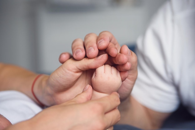 Os pés de um recém-nascido nas mãos dos pais. A mãe e o pai abraçam as pernas do bebê.