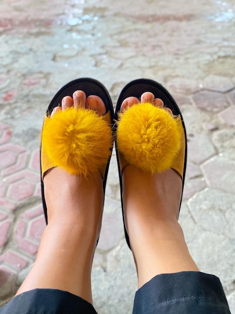 Os pés de uma mulher com pompons sobre eles, calçando um par de sandálias pretas.