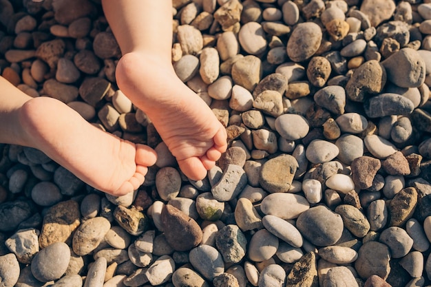 Os pés descalços de um bebê em uma praia de seixos