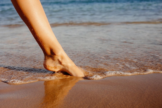 Os pés descalços de uma mulher ficam na praia em frente ao oceano.