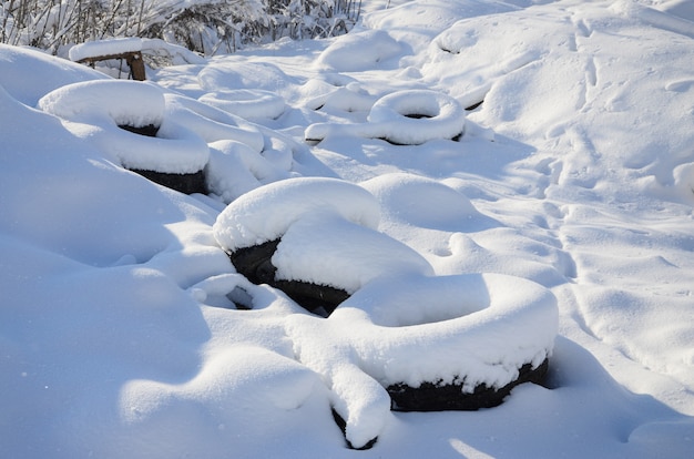 Os pneus de carro usados e descartados ficam ao lado da estrada, cobertos por uma espessa camada de neve