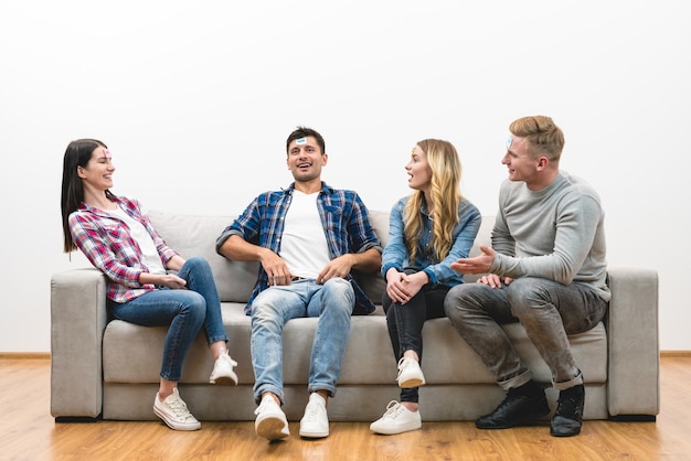 Os quatro amigos felizes no sofá jogam no fundo da parede branca