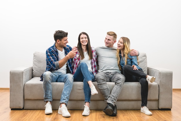 Os quatro amigos felizes sentam-se no sofá sobre um fundo branco de parede