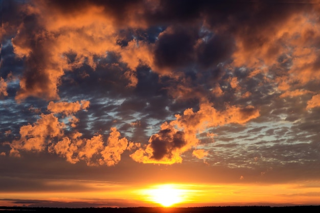 Os raios do sol poente no fundo de um céu dourado com nuvens laranja escuras uma paisagem de primavera