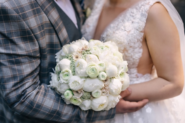 Os recém-casados estão segurando um lindo buquê de rosas brancas e peônias. fechar-se.